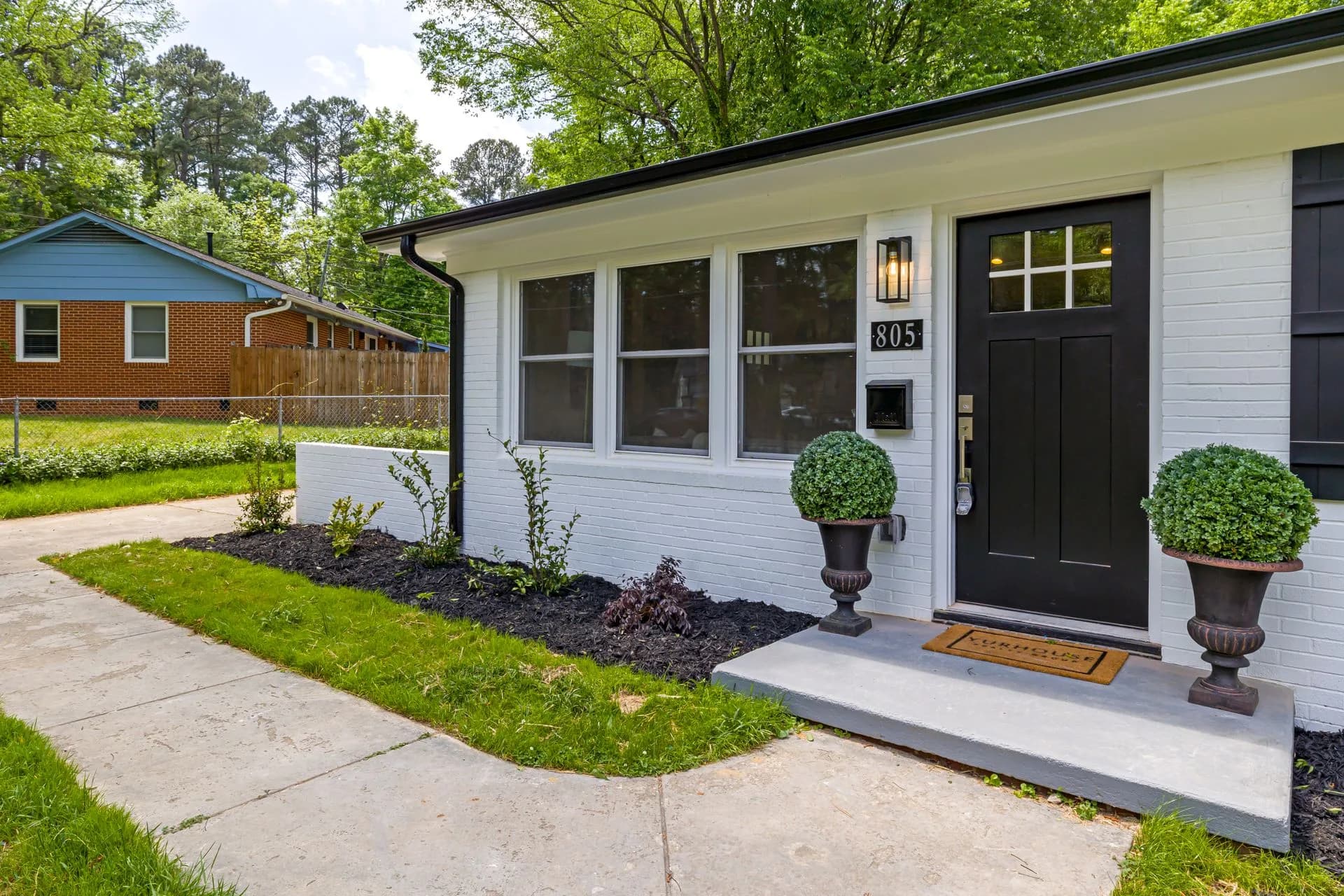A renovated single-story house exterior with a black front door and landscaped entry