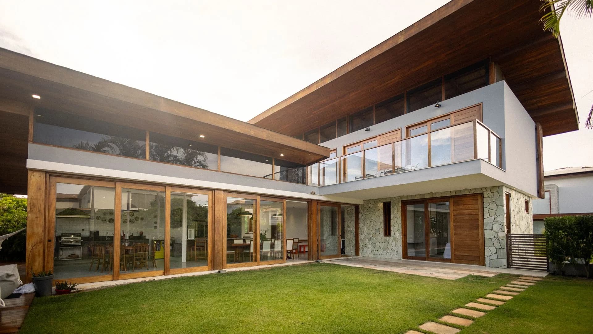 A modern architectural home with large glass windows and wood detailing surrounded by mature trees